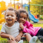 Toddlers Playing in Summer Heat; Playset in Background