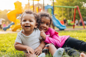 Toddlers Playing in Summer Heat; Playset in Background