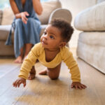 Baby crawling on hands and knees across a living room floor